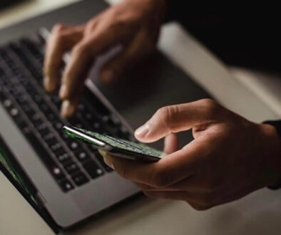 Någon som skriver på sin laptop och håller i en mobil samtidigt