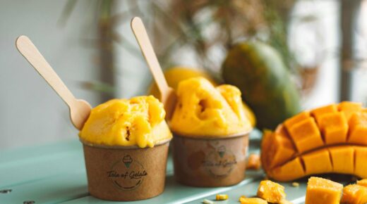 Två bägare med mango Gelato, en fint skuren mangohalva bredvid