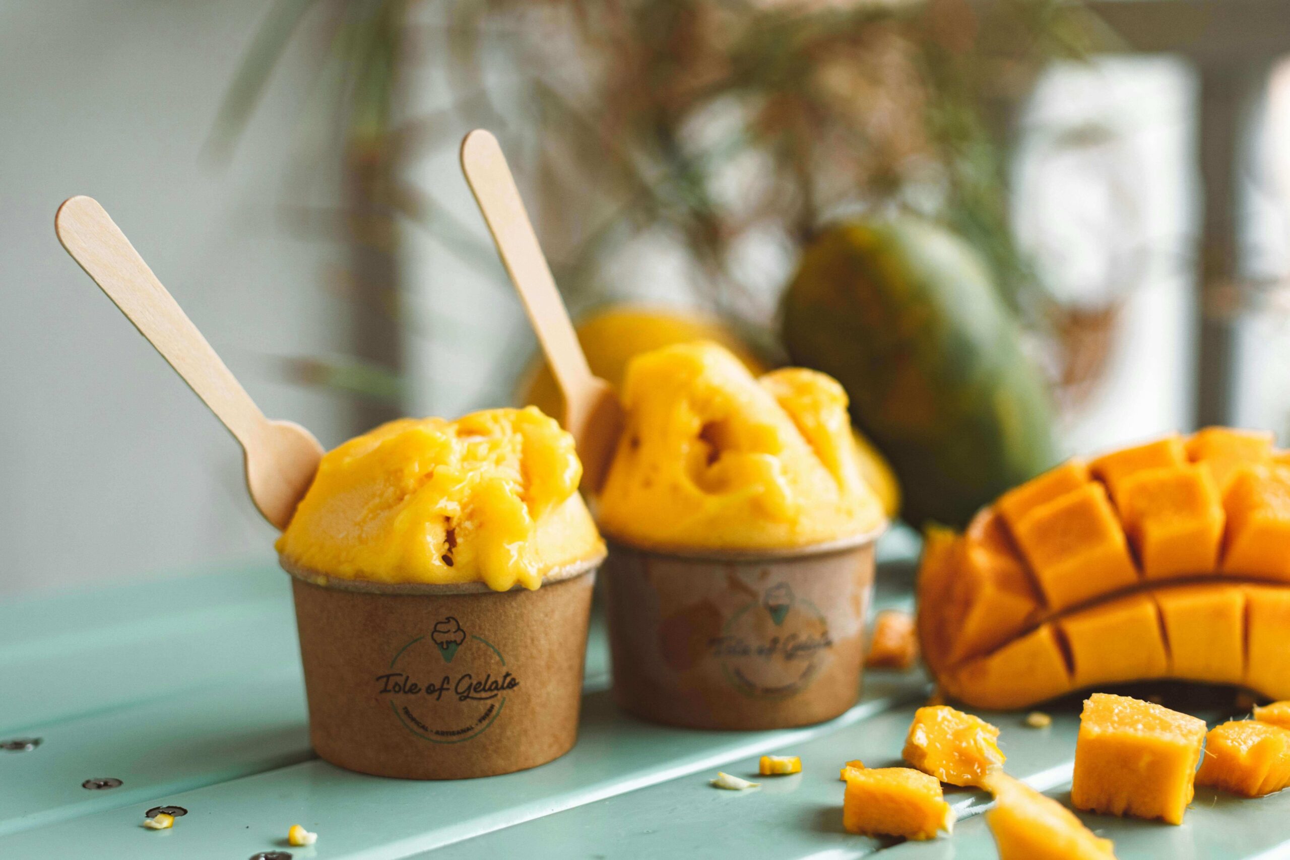 Två bägare med mango Gelato, en fint skuren mangohalva bredvid