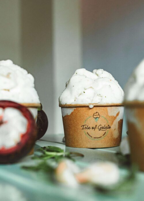 Tre bägare med gelato står på ett blått bord med frukter i förgrunden