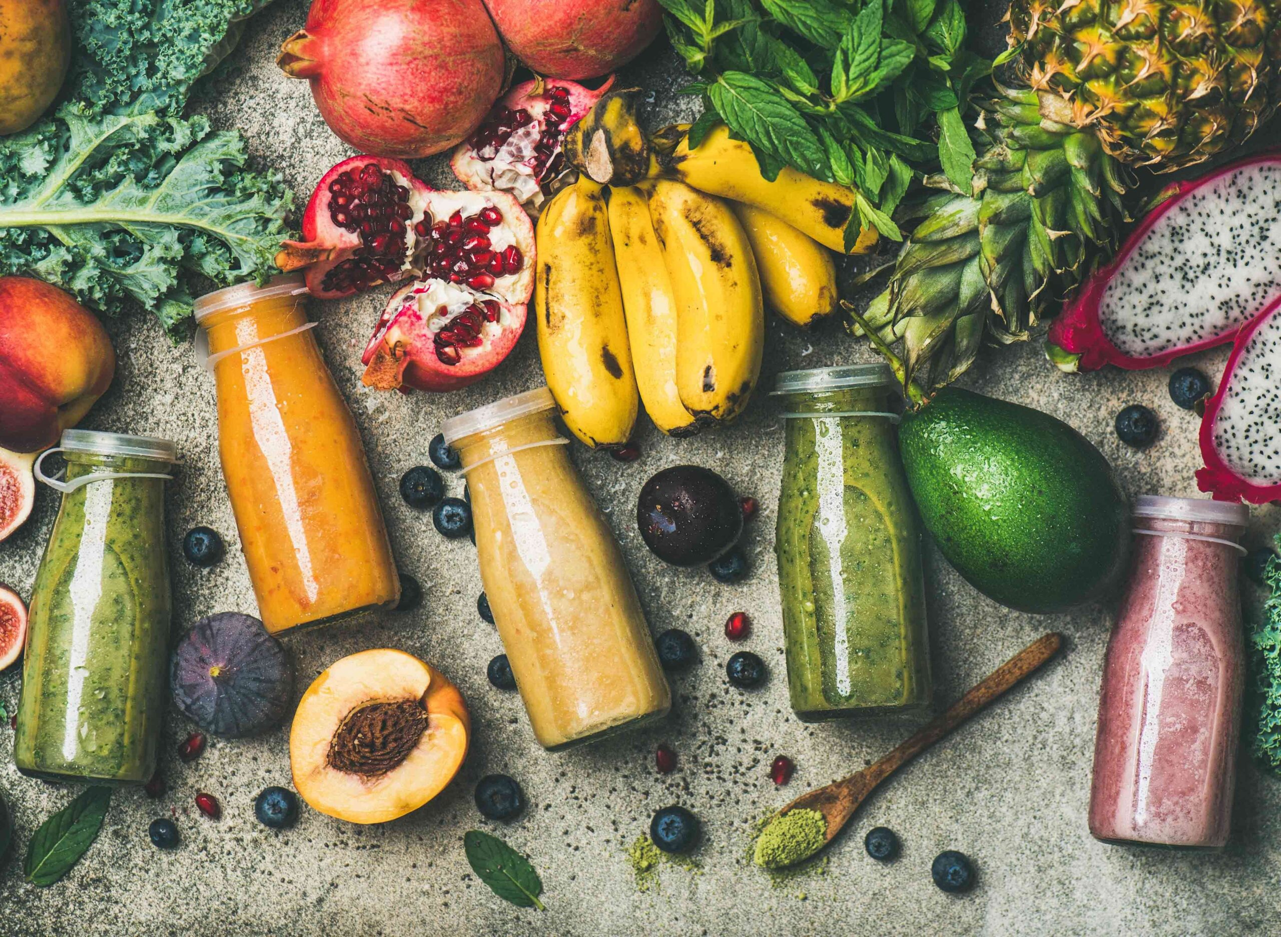Olika frukter utspridda tillsammans med fem flaskor med smoothies